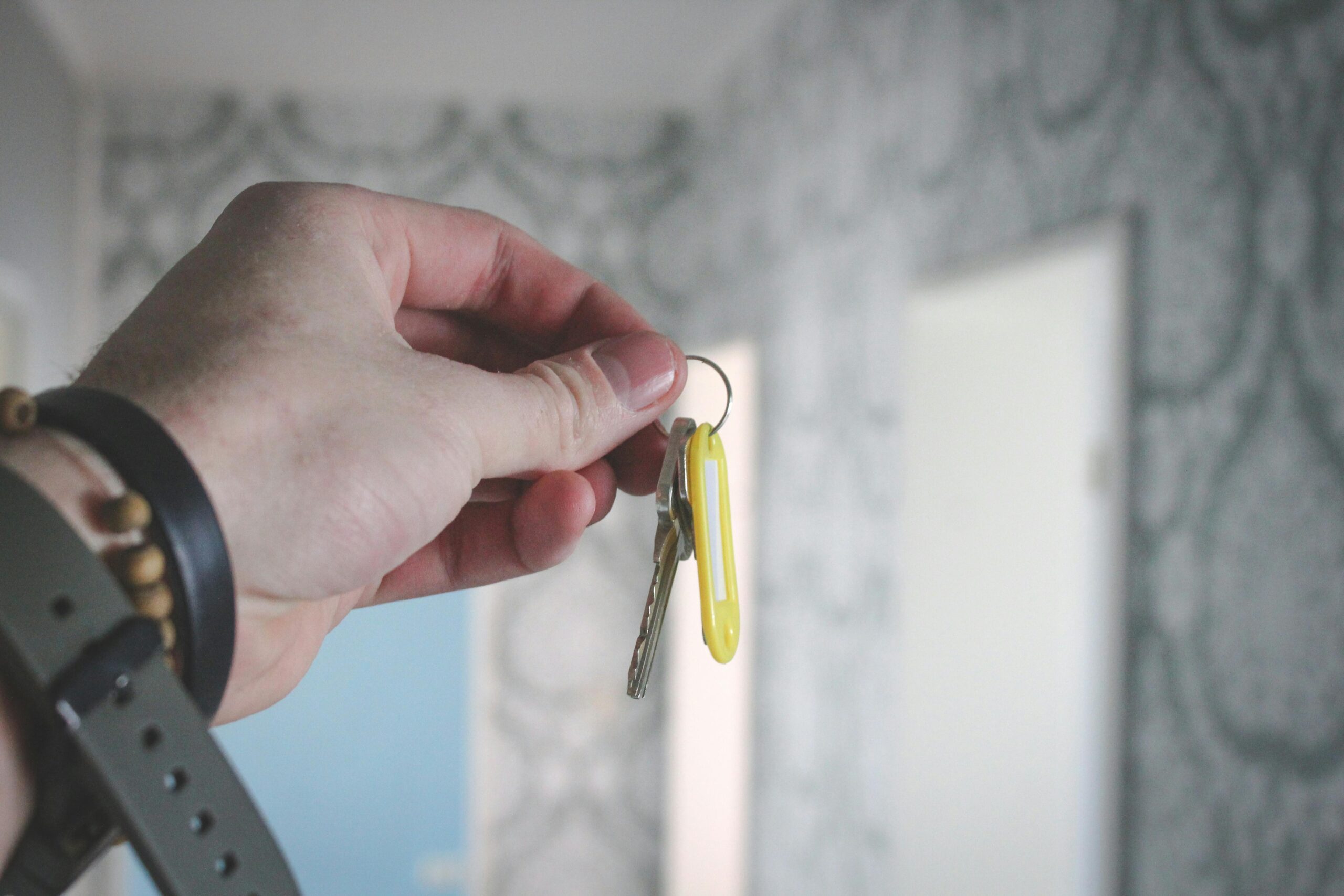 Projetos A hand holding a key against a blurred background of patterned wallpaper indoors.