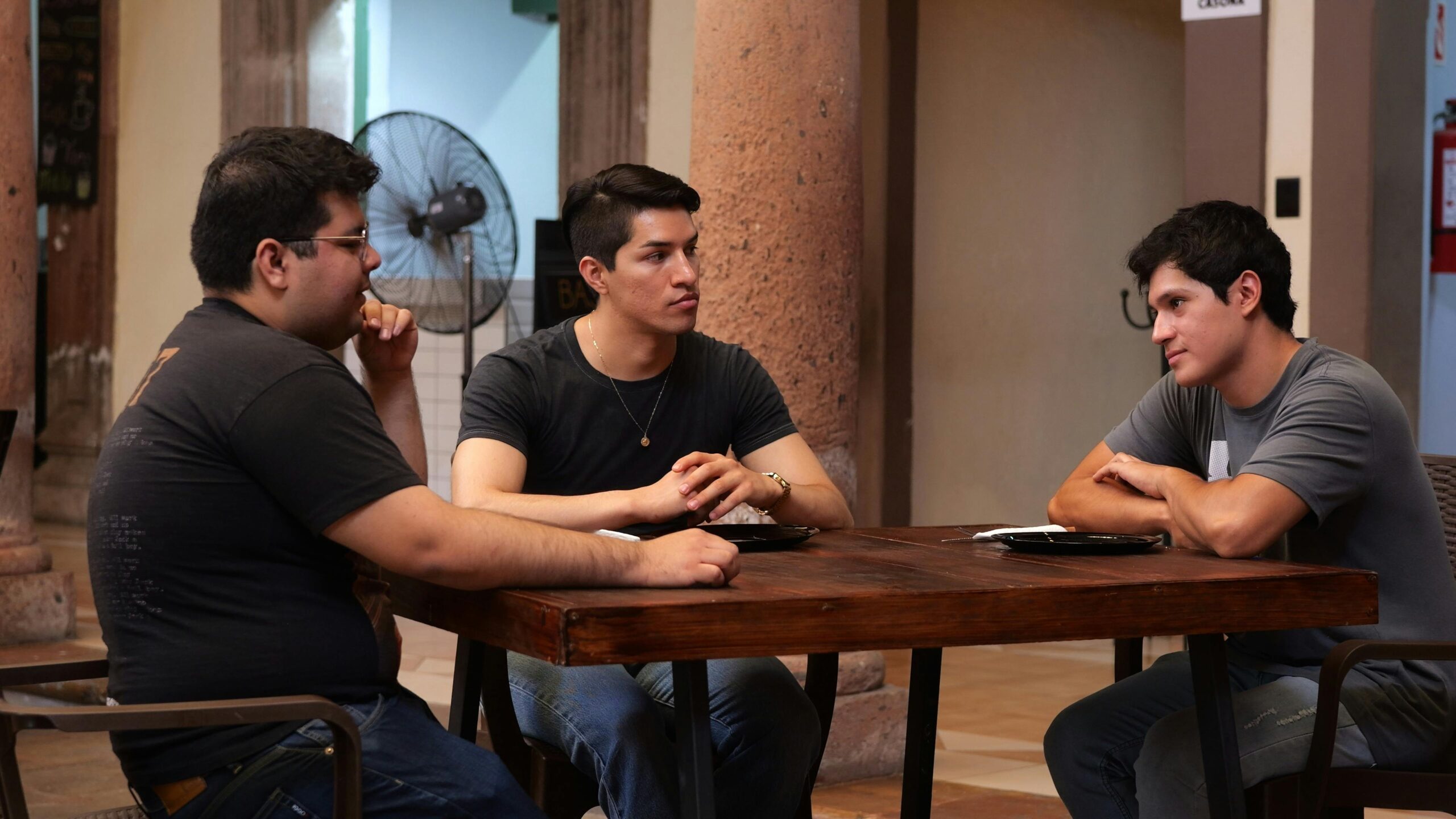Projetos Three men having a casual conversation at an indoor table in Guanajuato, Mexico.